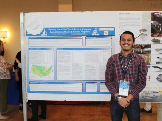 Person poses in front of their presentation at symposium